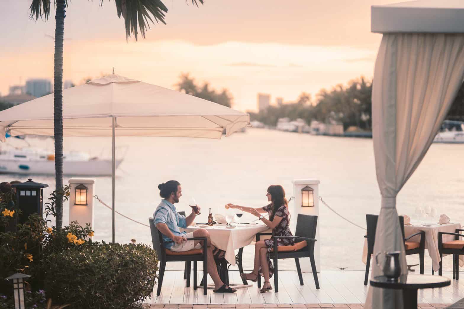 couple sitting at a waterfront restaurant table at sunset