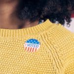 shot of woman's yellow sweater with I Voted sticker